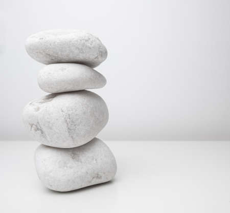 Tall stack of white stones or pebbles on white table with white wall background