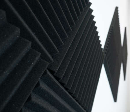 Black acoustic tiles on a white wall. Close up, shallow depth of field with focus in foreground.