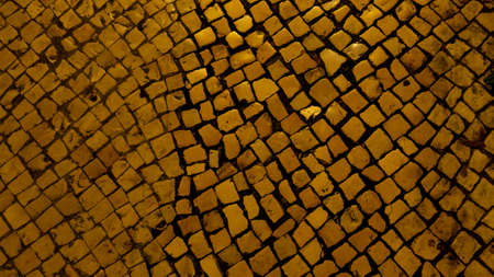 Portuguese sidewalk at night with traditional cobblestones, lit by yellow street lamp.の写真素材