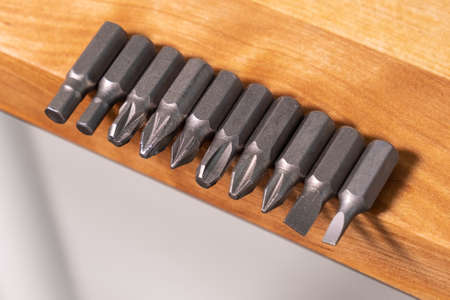 Several different screwdriver bits on the edge of solid wood workbench. Close up from above.