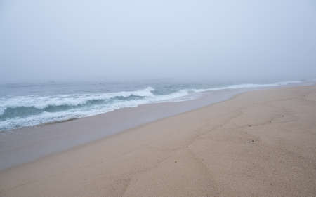 Thick, dense fog over ocean as waves break on empty, sandy beach.の写真素材