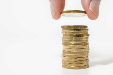 Building a stack of gold Euro coins on a white desk, holding a coin between finger and thumb.