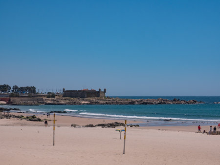 Beach in Matosinhos, Porto, Portugal with beach volleyball net foreground and Cheese Castle fort in backgroundのeditorial素材