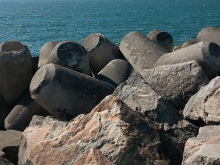 Breakwater made of boulders, rocks and moulded concrete with blue ocean water in backgroundの写真素材
