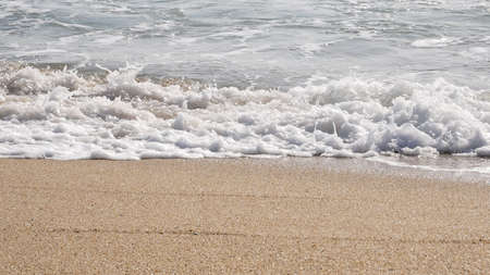 Close up of white foamy waves breaking on sandy beach