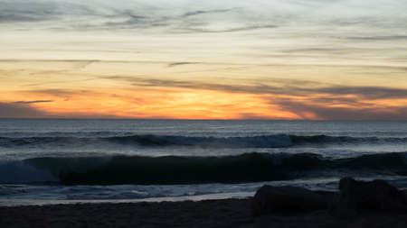 Sunset on Faro beach, Algarve, Portugal with dramatic sky and silhouetted rocks.
