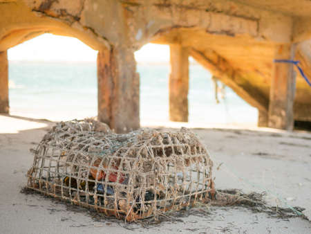 Old lobster pot on sandy beach in Algarve, Portugal in summer with jetty and sea in the background.の写真素材
