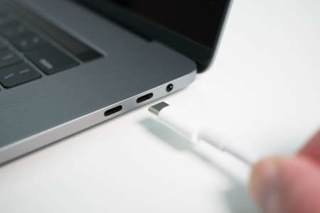 White USB-C or Type C cable being plugged in to a USB port on a grey laptop notebook computer.の写真素材