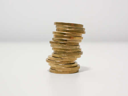 Uneven stack of gold colored Euro coins on a white desk about to topple overの写真素材
