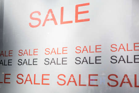 Large poster with the word SALE in bold letters in red and black, in a shop windowの写真素材