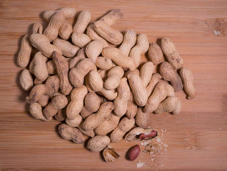 Pile of peanuts in shell with one shell opened, on natural wooden background.の写真素材