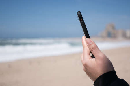 Woman's hands holding and using smartphone on beach in summerの写真素材