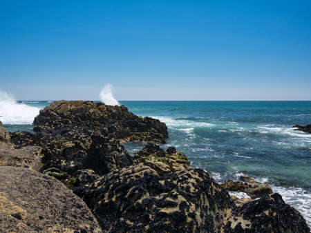 Natural rocky beach in Povoa de Varzim, Portugal on a bright summer day with waves crashing onto rocksの写真素材