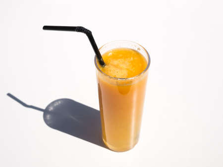 Glass of orange juice with straw casting shadow on white tableの写真素材