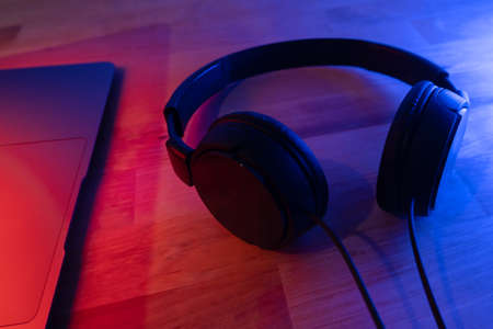 Black headphones on wooden desk with colored lighting