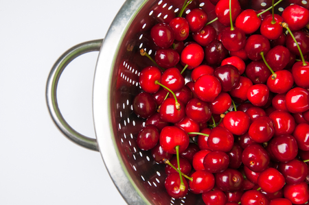 fresh cherries in colander on white backgroundの写真素材