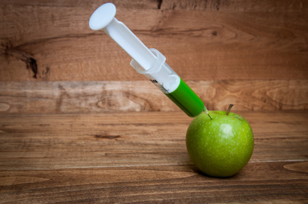 GMO apple with syringe on wooden backgroundの写真素材