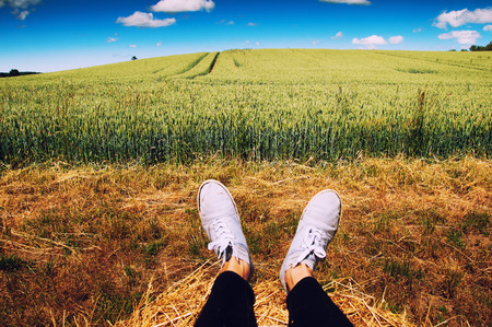Woman's legs with blue shoes sitting on a baleの写真素材