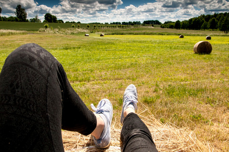 Woman's legs with blue shoes sitting on a baleの写真素材