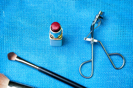 Red lipstick, eyelash curler and brushes on blue backgroundの写真素材