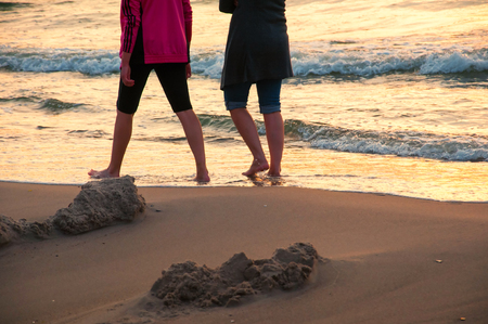 Two girls walking on the beach in sunset timeの写真素材