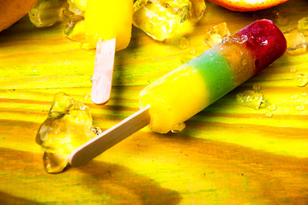 Colorful ice lolly and friuts on green wooden background