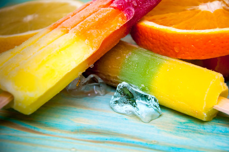Colorful ice lolly and friuts on blue wooden background