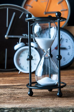 Hourglass and ticking clocks on old wooden tableの写真素材