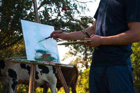 Man painting a picture of cows in the open airの写真素材