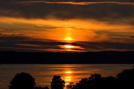 Beautiful sunset on a lake. The sun disappears behind the clouds.の写真素材