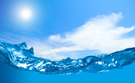 Blue water wave with shallow depth of field and cloudy sky with sun in the backgroundの写真素材