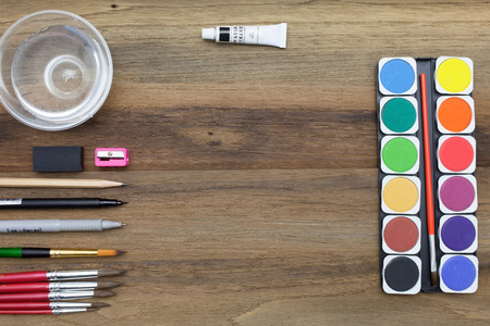 Workstation concept top view : Water color,brush,pen,marker,pencil,rubber,glass of water on wooden backgroundの写真素材