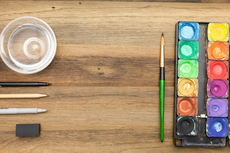 Workstation concept top view : Water color,brush,pen,marker,pencil,rubber,sharpener,glass of water and color pencil on wooden backgroundの写真素材