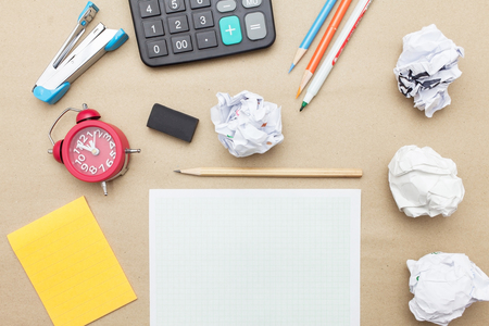 Business concept:Calculator,stapler,red clock,white blank paper,crumpled paper,post it and color pencil,pencil,pen on brown paper backgroundの写真素材