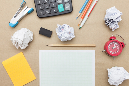 Business concept:Calculator,stapler,red clock,white blank paper,crumpled paper,post it and color pencil,pencil,pen on brown paper backgroundの写真素材