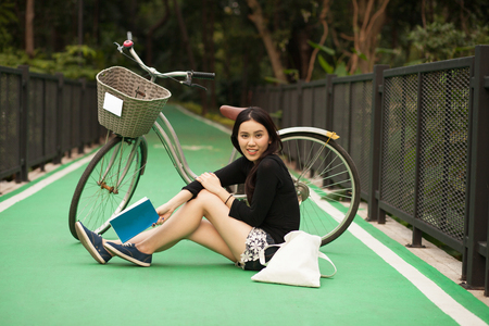 Pretty Thai girl reading book and sitting near by bicycle at the parkの写真素材