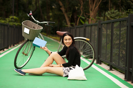 Pretty Thai girl reading book and sitting near by bicycle at the parkの写真素材