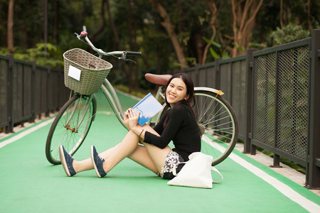 Pretty Thai girl reading book and sitting near by bicycle at the parkの写真素材