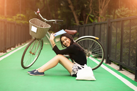 Pretty Thai girl reading book and sitting near by bicycle at the parkの写真素材