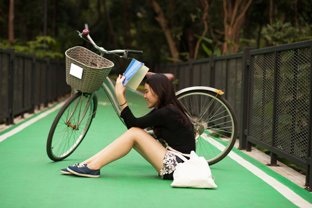 Pretty Thai girl reading book and sitting near by bicycle at the parkの写真素材