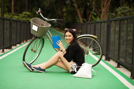 Pretty Thai girl reading book and sitting near by bicycle at the parkの写真素材