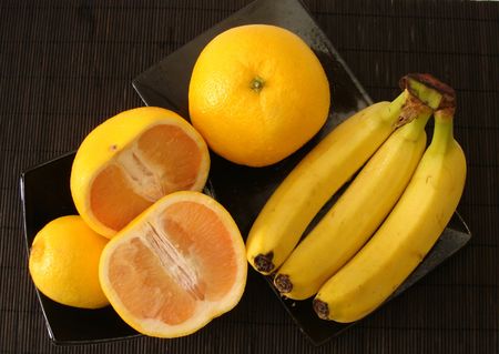 orange, lemon and banana on black plates の写真素材