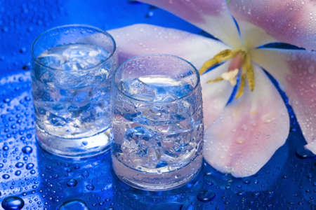 Glasses with water and flower over blue