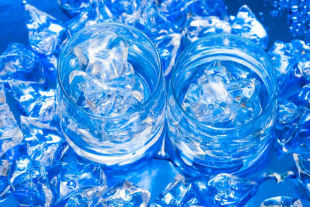 Glasses with water and ice over blue の写真素材