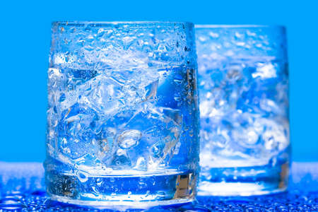 Glass with water and ice over blue の写真素材