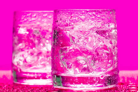 Glass with water and ice over pink の写真素材