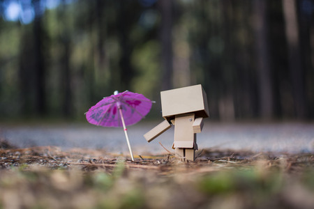 Robot toy and umbrella on the road with the pine forest in the backgroundの写真素材