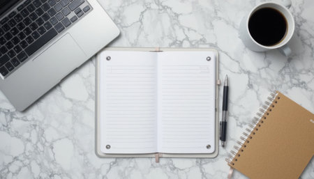 A neat workspace featuring a laptop, an open notebook, a pen, and a cup of coffee on a marble surface.の素材