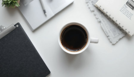 A coffee cup on a tidy desk with a pen, notebook, and plant creates a cozy workspace vibe.の素材