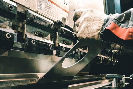 Worker on an old machine bends metal. Old machine tool at the factory. Worker bends parts in the darkの写真素材